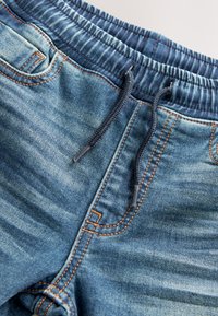 Kék farmer jogger nadrág elasztikus derékpánttal és fekete húzózsinórral, narancssárga varrással és első zsebekkel.