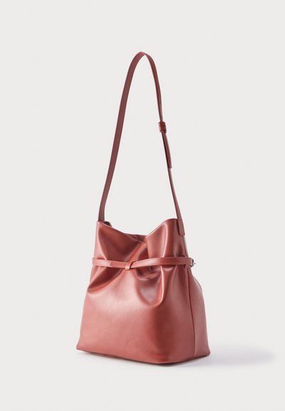 Sac à bandoulière en cuir rose doux avec une longue sangle réglable et un détail de ceinture horizontale autour du milieu, présenté sur un fond uni.