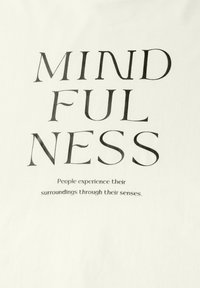 Bílá tkanina s výrazným černým textem, který zní "MINDFULNESS" ve velkém písmu nad menším textem: "Lidé zažívají své okolí prostřednictvím svých smyslů."