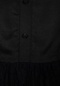 Svart klänning med en slät satinöverdela och knappstängning, som övergår till en texturerad spetskjol. Subtil lyster genom hela tyget.