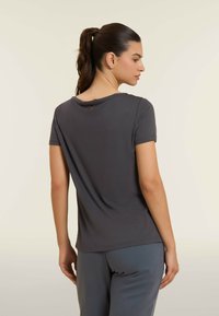 Camiseta gris con cuello redondo y mangas cortas, hecha de tela suave. Presenta un pequeño detalle de botón rojo en la parte posterior.