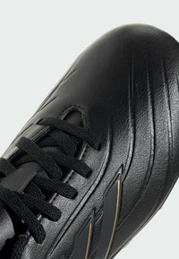 Zapato de fútbol negro con una parte superior de cuero liso con textura en relieve, cordones negros y detalles dorados en el lateral. Forma aerodinámica diseñada para el rendimiento.