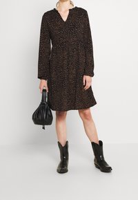 Svart klänning med leopardmönster, långa ärmar och V-hals. Matcher med svarta cowboystövlar och en svart dragsko väska.