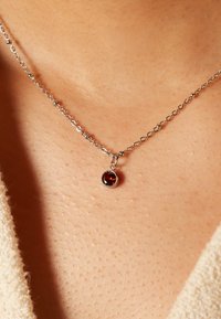 Zilveren ketting met een kleine ronde rode edelsteen hanger, met een gepolijste afwerking en een eenvoudig sluitingontwerp.