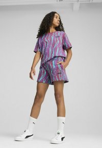 Conjunto atlético de top y pantalones cortos con un patrón en tonos morados y verdes azules, que presenta mangas cortas y una cinturilla elástica. Zapatillas y calcetines blancos complementan el look.