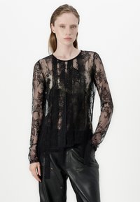 Black lace long-sleeve top with floral patterns, sheer texture, round neckline, and flowing design. Paired with black leather trousers.