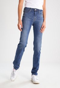 Jeans de mezclilla azul con un ajuste slim, diseño de cinco bolsillos y un ligero desvanecimiento. Presentan un cierre de botón y pasadores para cinturón en la cintura.