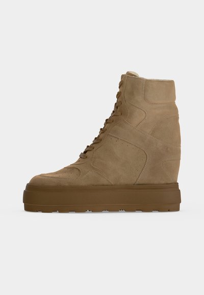 Μπεζ sneaker υψηλής κορυφής από σουέντ με χοντρή καφέ λαστιχένια σόλα και κορδόνια μπροστά, απεικονίζεται από το πλάι σε απλό φόντο.