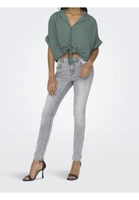 Groene shirt met korte mouwen, geknoopt in de taille, gecombineerd met lichtgrijze skinny jeans en zwarte hoge hakken. Glad stof, casual ontwerp.