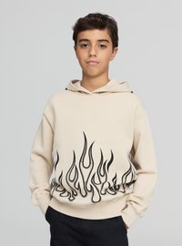 Beżowa bluza z kapturem z abstrakcyjnym czarnym wzorem płomieni na dolnej połowie. Posiada kaptur ze sznurkiem i ściągacze przy mankietach. Gładka tekstura materiału.