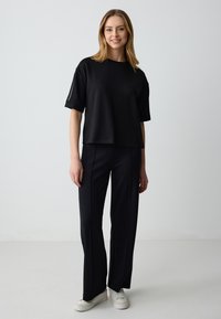 Zwart cropped t-shirt met korte mouwen, gecombineerd met zwarte wijde broek. De outfit heeft een gladde textuur en een minimalistisch ontwerp.
