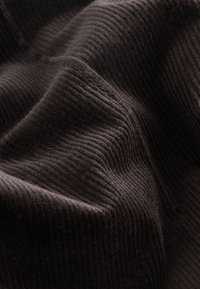 Il tessuto di velluto a coste marrone scuro presenta righe verticali prominenti, con una texture soffice e una leggera lucentezza, creando una profonda ricchezza visiva.