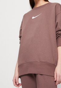 Sudadera de Nike en color malva con logo blanco, que presenta un corte relajado, puños y dobladillo de canalé, textura suave y escote ancho.