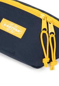 Astuccio blu navy con zip e tiranti gialli, realizzato in tessuto texturizzato. Presenta un'etichetta gialla Eastpak sul lato.