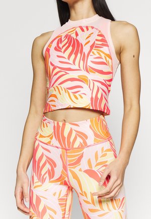 Vrouw draagt een mouwloos, nauwsluitend crop top en legging met een levendig patroon van roze, oranje en gele abstracte bladeren.