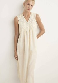 Vestido largo sin mangas de tela color crema con escote en V, bordado intrincado a lo largo del corsé y una silueta relajada y fluida.