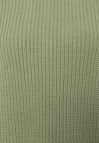 Gros plan sur un tissu tricoté vert clair avec une texture côtelée verticale et des points de fil doux visibles.