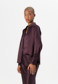 Satin blouse and skirt set in deep purple. Tailored fit, buttons down the front, and long sleeves. Smooth texture with a sleek design.
