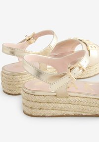 Gouden metallic platform sandalen met een espadrille-achtige geweven jute zool, voorzien van een gespstrap en een zachte roze binnenzool.