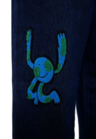 Jeans en denim avec un design bleu et vert brodé représentant un personnage stylisé sur la jambe gauche. Tissu bleu marine foncé avec une texture subtile.