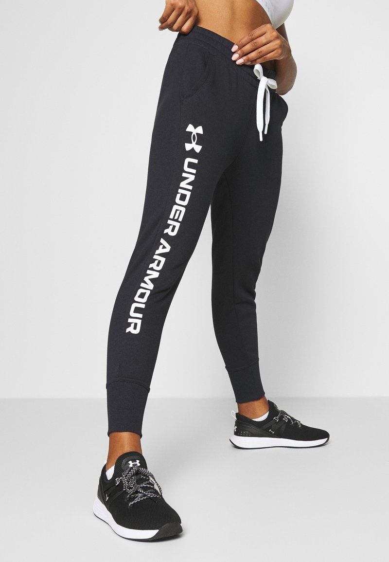 Marinblå joggarbyxor med vitt "UNDER ARMOUR"-logotyp, elastisk midja, snörning och muddar vid anklarna, i kombination med svarta träningsskor.