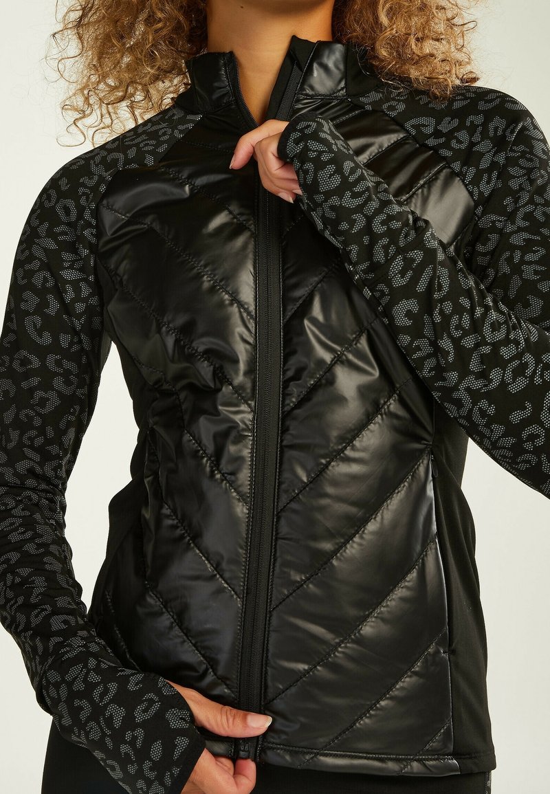 Giacca sportiva nera con un frontale lucido e trapuntato a motivo chevron e maniche lunghe con un sottile design a stampa leopardata.