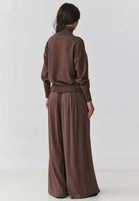 Brązowy sweter z golfem, z prążkowanym dołem i luźnym krojem, w połączeniu z brązowymi spodniami o szerokich nogawkach, charakteryzującymi się gładką, płynącą fakturą.