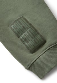 Mankiet w kolorze oliwkowym z naszywaną prostokątną łatą z napisem "WIELKA ZIELEŃ" dużymi, pionowymi literami.