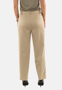 Pantaloni beige su misura con una texture liscia, design a gamba dritta, tasche posteriori e vita a media altezza, abbinati a tacchi alti neri.