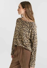 Maglione in stampa leopardata beige con scollatura ampia e maniche lunghe, abbinato a pantaloni marroni con texture e plissettati.