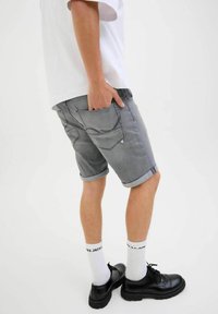 Grijze denim shorts met opgerolde zoom, achterzakken en een gladde textuur, gecombineerd met zwarte schoenen en witte crew-sokken.