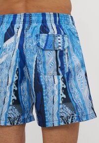 Blue patterned swim shorts featuring horizontal stripes in various shades of blue, with an elastic waistband and a rear pocket detail.