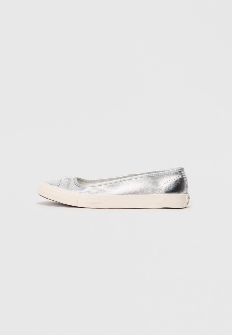 Silberne metallische flache Schuhe mit runder Spitze, beiger Gummisohle und einem kleinen Schleifendetail an der Vorderseite. Glatte Textur und minimalistisches Design.