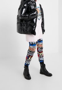 Černá lesklá péřová bunda, světle růžové oversized tričko a legíny s multikolorním potiskem spárované s černými kotníkovými botami se zipy.