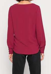 Burgundská blůza s dlouhými rukávy, kulatým výstřihem a knoflíkovými manžetami, vyrobená z měkké tkaniny s hladkou strukturou. Zobrazeno ze zadní strany.