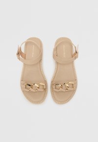 Beige sandaler med flettede stropper og gullfargede detaljer. Justerbar ankelrem; minimalistisk design og myk tekstur.
