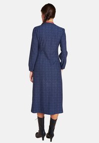 Marineblaues langärmliges Kleid mit strukturiertem Muster, das bis zur Mitte der Wade reicht, kombiniert mit kniehohen schwarzen Stiefeln.