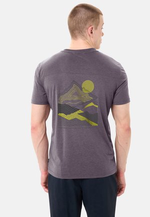 Uomo di spalle che indossa una maglietta grigia con una grafica sul retro raffigurante una montagna con linee di contorno gialle e nere e un sole.