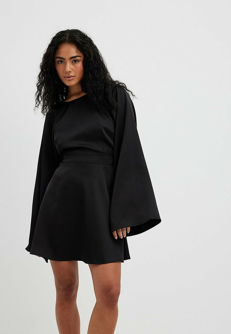 Robe noire avec de longues manches cloche, texture satin lisse, taille cintrée et jupe évasée. Encolure ronde simple, sans motifs ni accents visibles.
