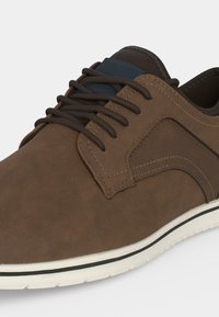 Chaussure décontractée marron à lacets marron foncé, panneau latéral texturé et semelle blanche avec bande noire, vue en angle avant latéral.