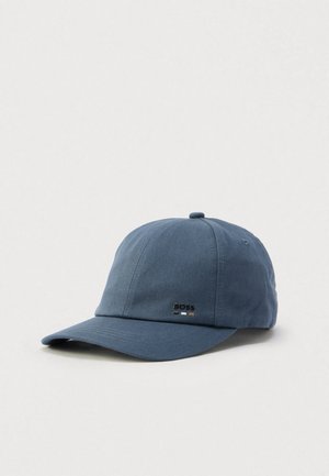 Gorra azul de algodón con visera curva, que presenta un detalle de logo metálico. El diseño es liso con paneles cosidos y un botón en la parte superior.