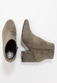 Botas de tobillo de ante verde oliva con puntera puntiaguda, cremallera lateral y tacón grueso negro. Textura suave y diseño casual.