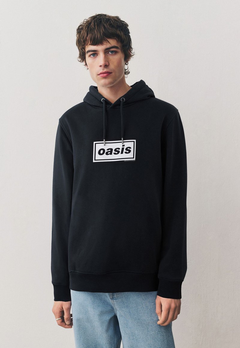 Zwarte hoodie met trekkoorden, voorzien van een prominent wit rechthoekig logo met de tekst "oasis" in het midden van de borst.