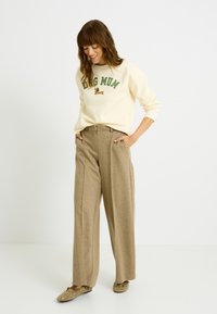 Sudadera cremosa con texto en verde "Dog Mum" y un gráfico de perro, combinada con pantalones de pierna ancha en marrón claro y zapatos de lona color canela con detalles de ojales.