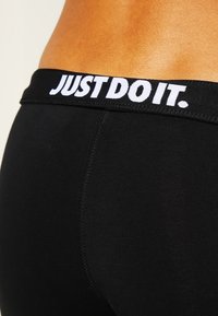 Černé sportovní legíny s širokým elastickým pasem s nápisem "JUST DO IT." v bílé barvě. Hladká textura a přiléhavý střih.