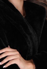 Sort faux fur omslag med en blød, glat tekstur og bred krave. Har en buet udskæring og et lagdelt design, der fremhæver varmen.