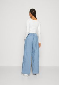 Pantalóny so širokými nohavicami v modrobielych prúžkoch s elastickým pásom. Nosia sa s bielym topom s dlhým rukávom, ktorý ukazuje uvoľnený strih.