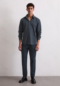Donkergrijze overhemd met lange mouwen, gecombineerd met bijpassende donkere broek en zwarte schoenen. Glad oppervlak, op maat gemaakte pasvorm, minimalistisch ontwerp.