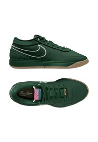 Grüne Turnschuhe mit einer strukturierten Musterung, Obermaterial aus Stoff, weißen Akzenten, Schnürdesign und einer Laufsohle aus Gummilaufsohle. Markenzeichen auf der Zunge.