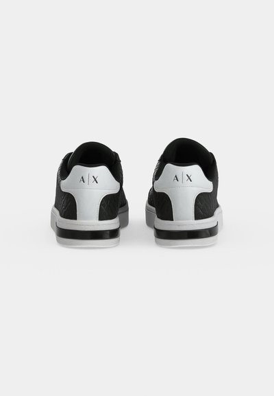 Vue arrière d’une paire de baskets noires avec des empiècements blancs au talon et des semelles blanches, ornées de logos A|X.